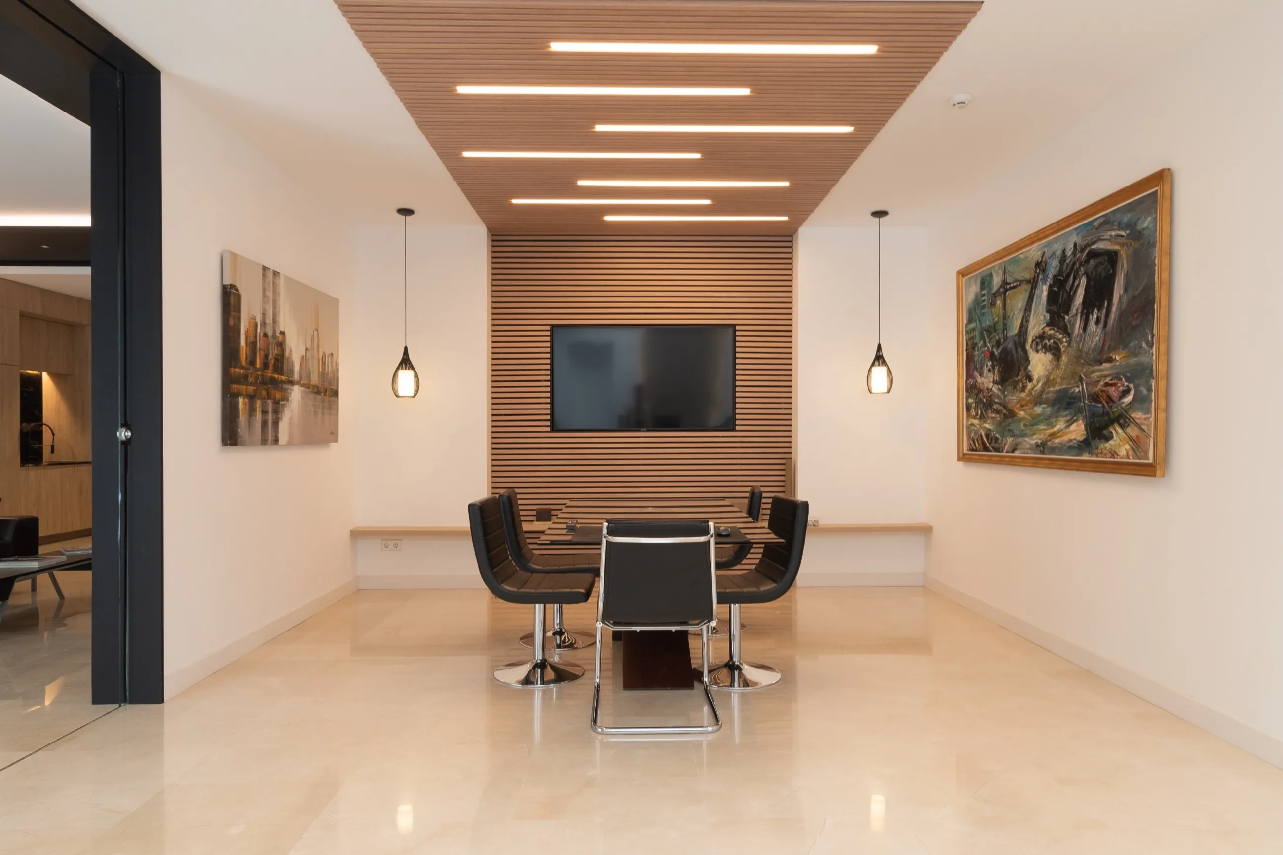 Sala de reuniones con techo de listones de madera, iluminación lineal y pinturas en las paredes
