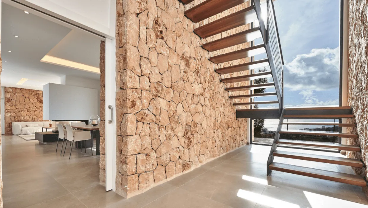 Escalera de peldaños de madera junto a un muro de piedra y ventana con vistas al mar en Génova