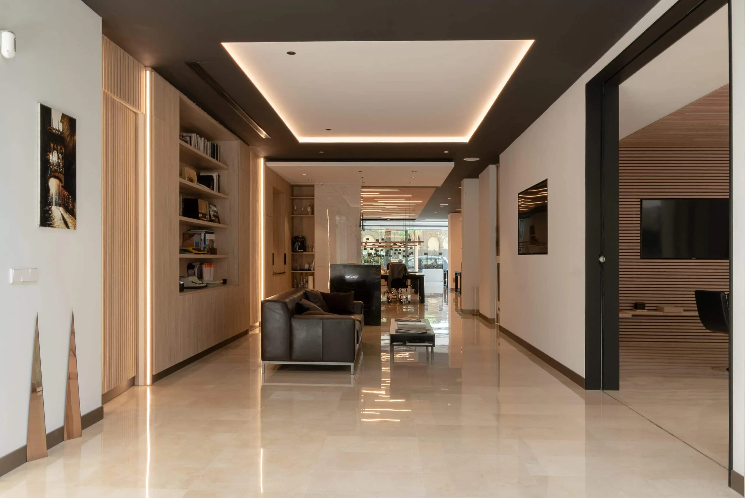 Pasillo de la oficina HOMEY con estanterías, falso techo iluminado y suelo de piedra pulida