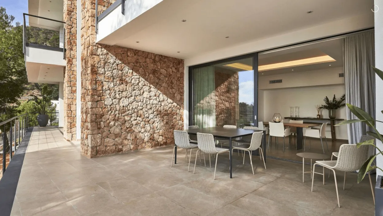 Terraza cubierta con comedor en la vivienda Hoff, con muro de piedra