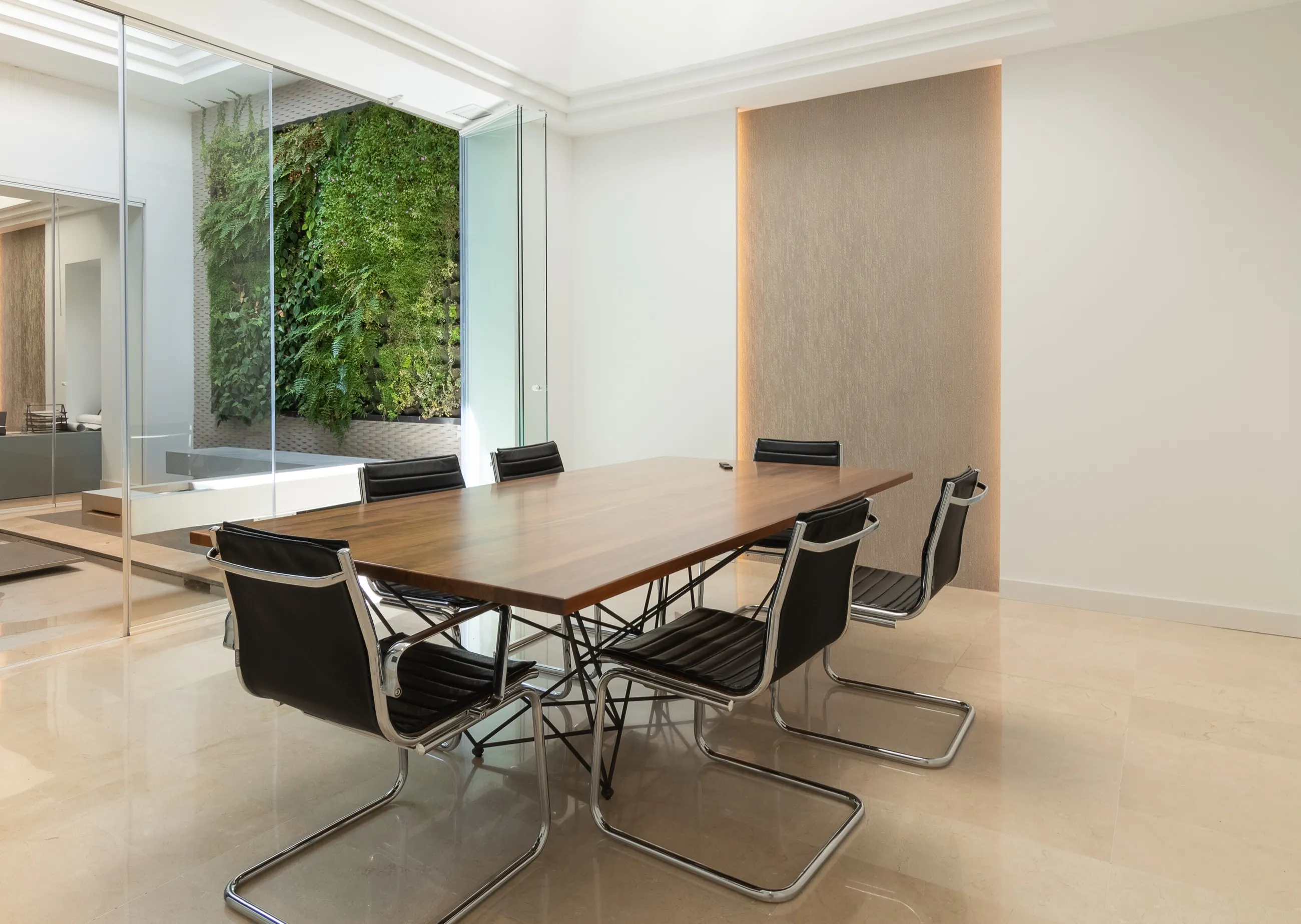 Mesa de reuniones de madera con sillas negras y el jardín vertical tras el cristal