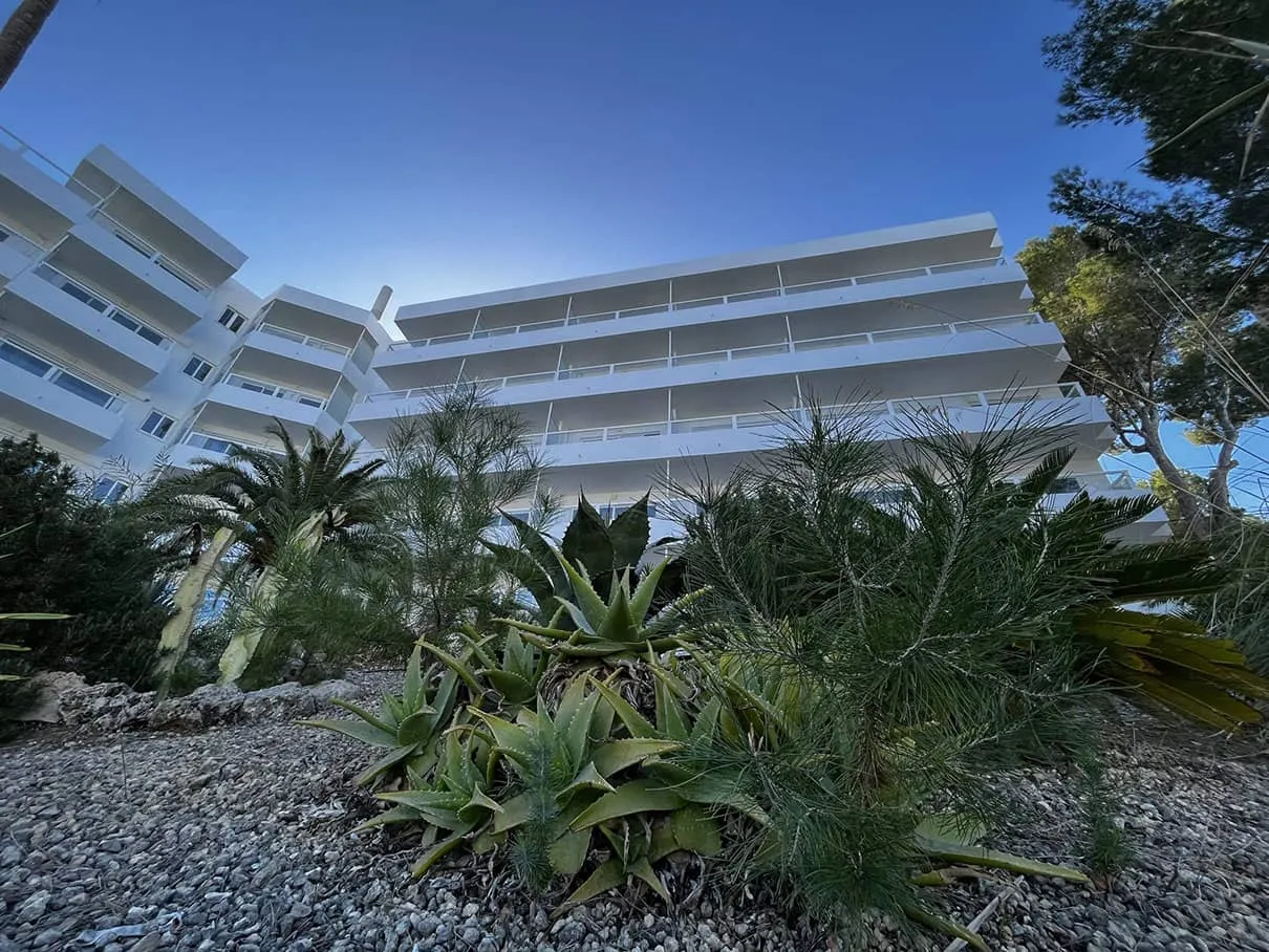 Fachada del Hotel Portofino tras la reforma, vista entre agaves y pinos, Santa Ponça