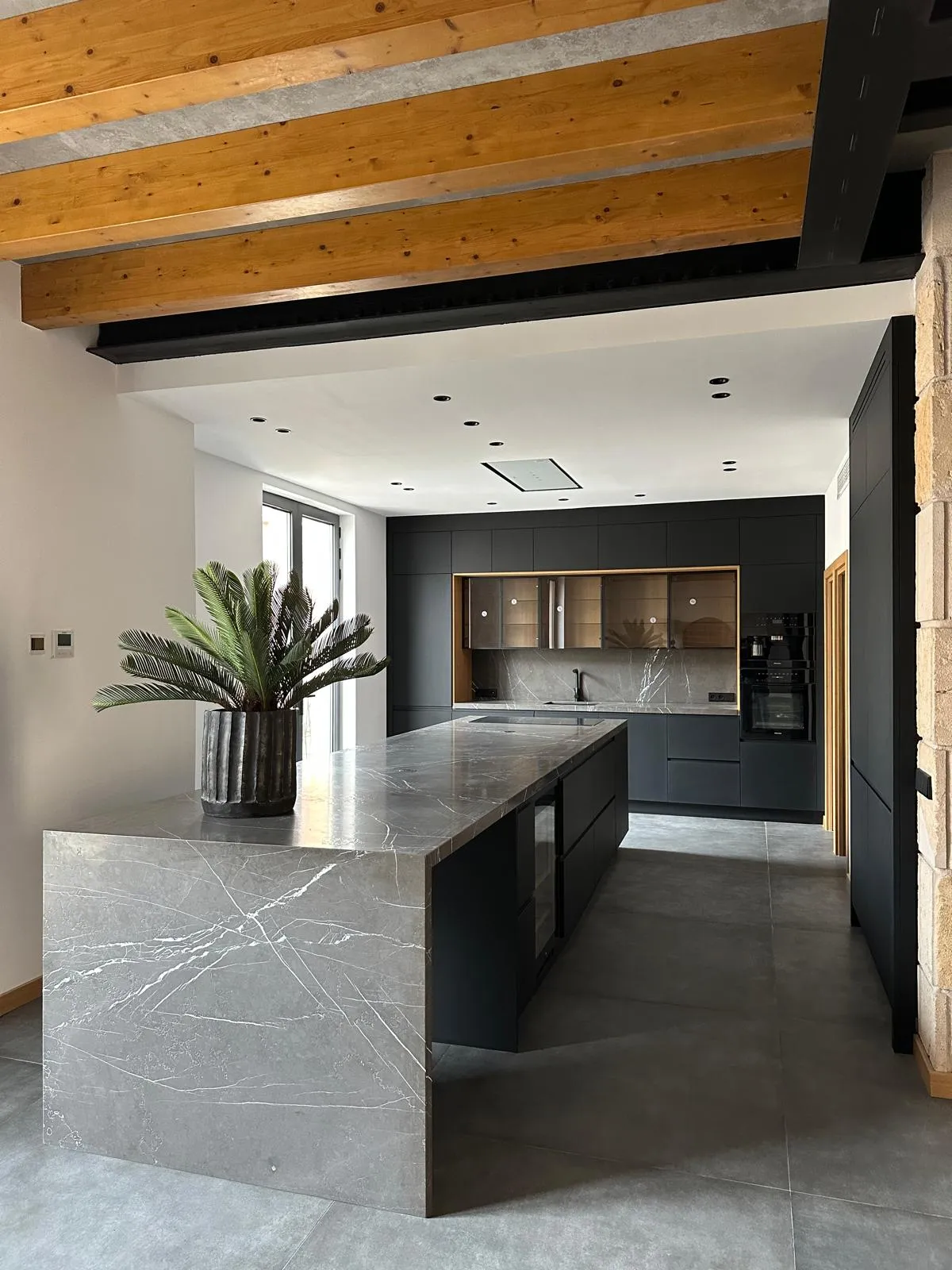 Cocina con isla de piedra y mobiliario negro mate en la vivienda Cotoner, Palma de Mallorca