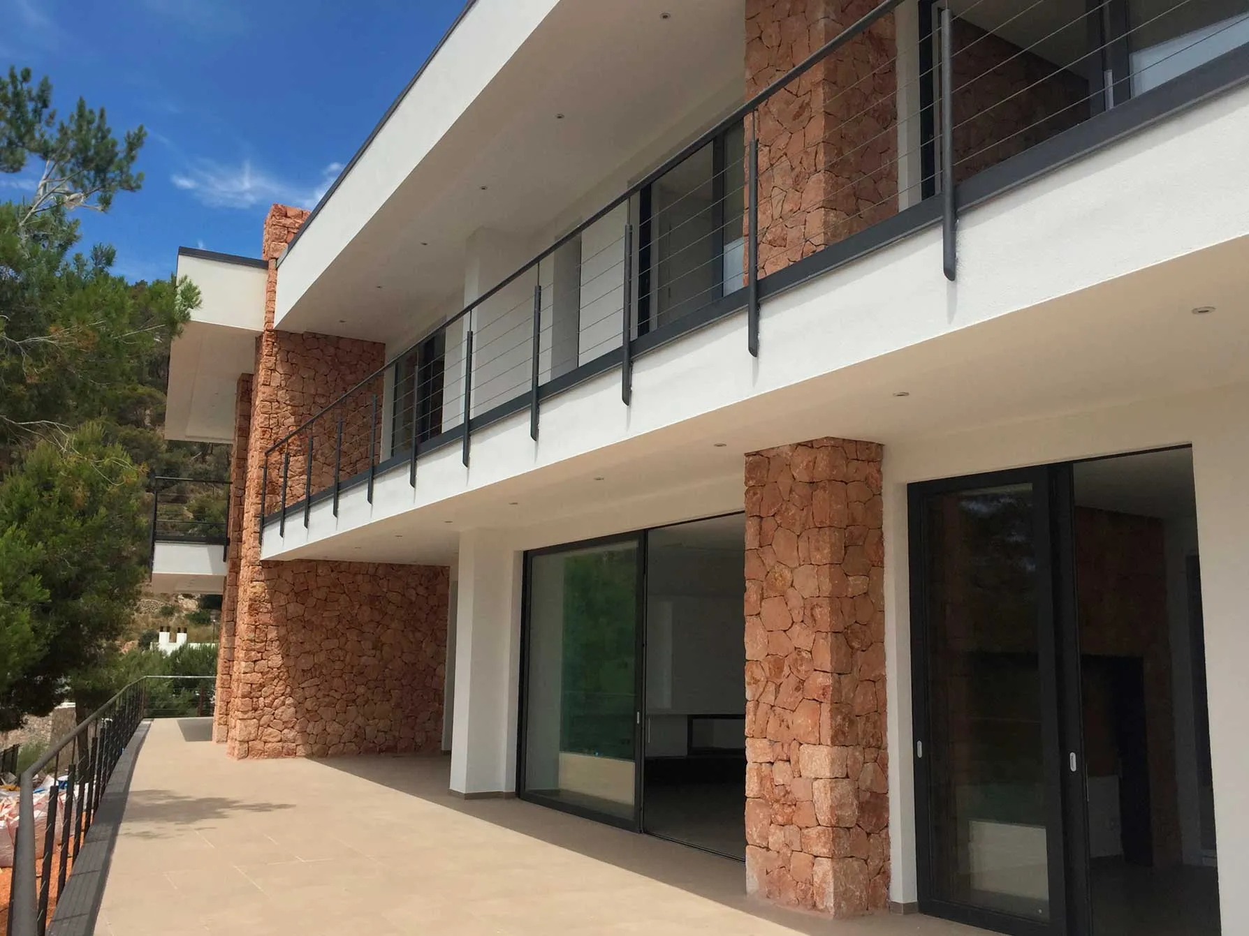 Fachada de la vivienda Hoff con pilares de piedra y barandilla de cables