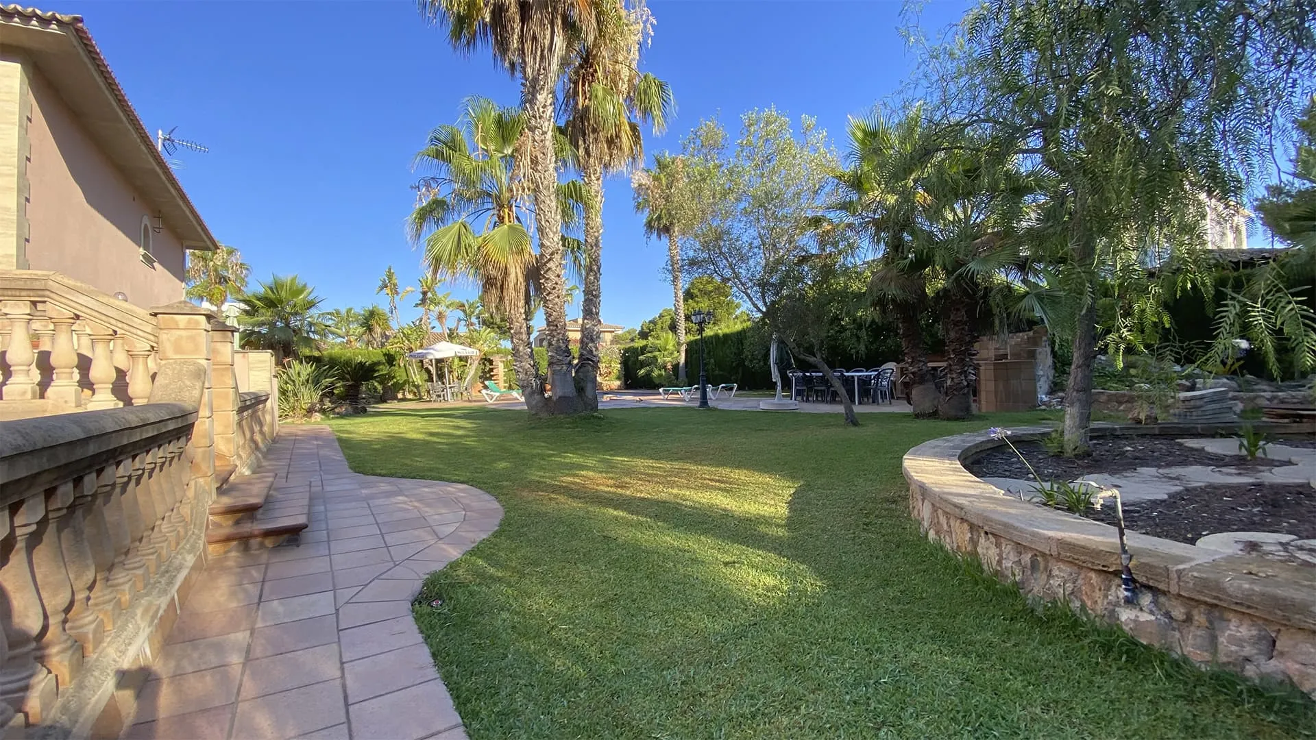 Jardín con camino de baldosa, césped y balaustrada en la vivienda Xiela de Bunyola, Mallorca