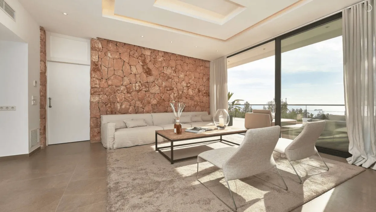 Salón de Génova con sofás claros, mesa baja y ventana panorámica sobre el entorno de Palma