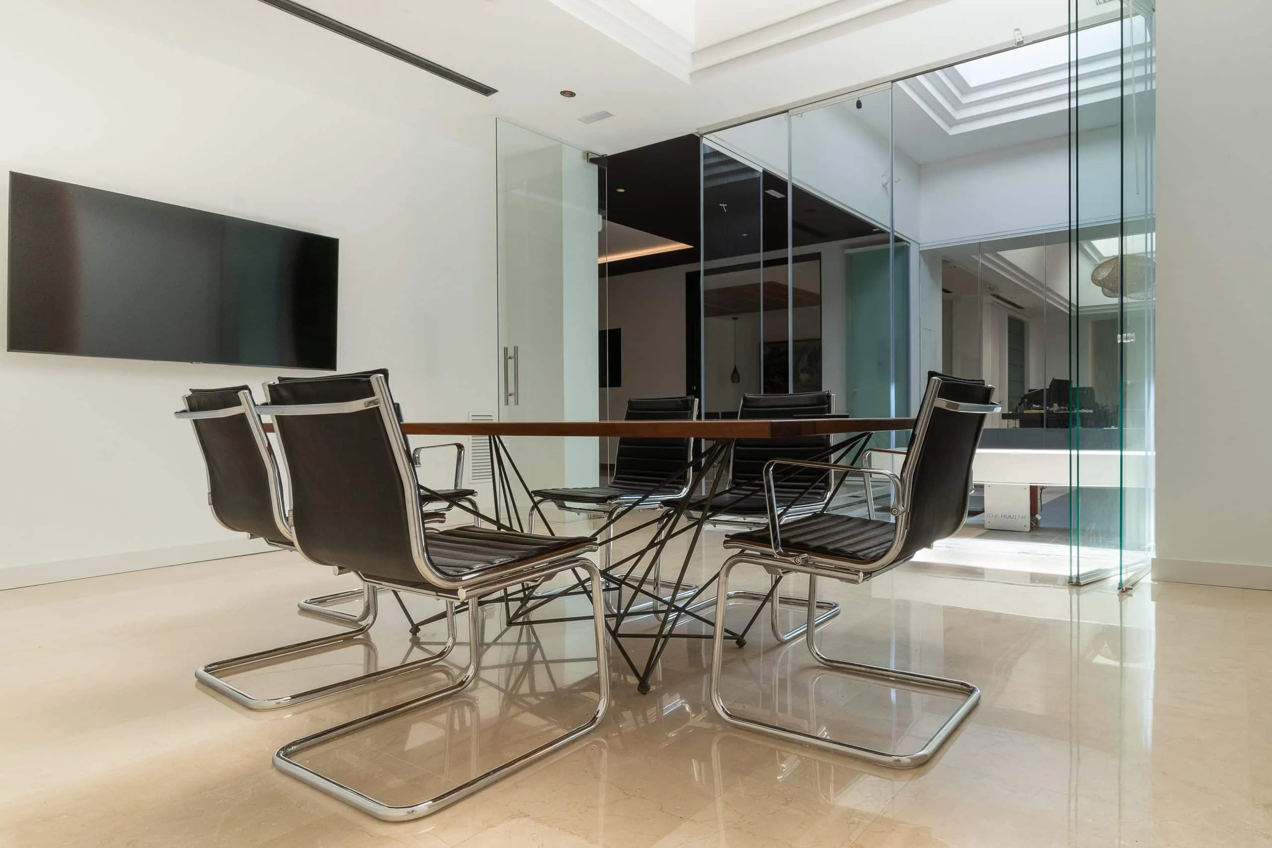 Sala de reuniones con paredes de vidrio y mesa de madera en las oficinas HOMEY, Palma