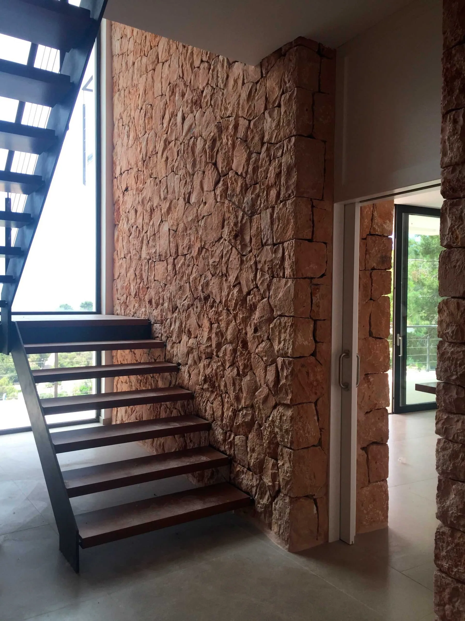 Escalera interior metálica junto a muro de piedra en la vivienda Hoff