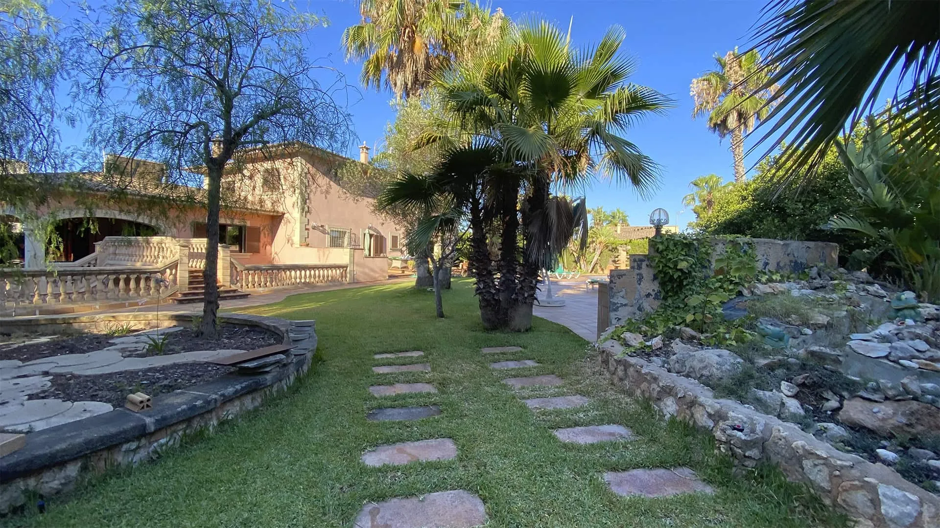 Jardín con palmeras, bancales de piedra y camino de losas en la vivienda Xiela, Bunyola