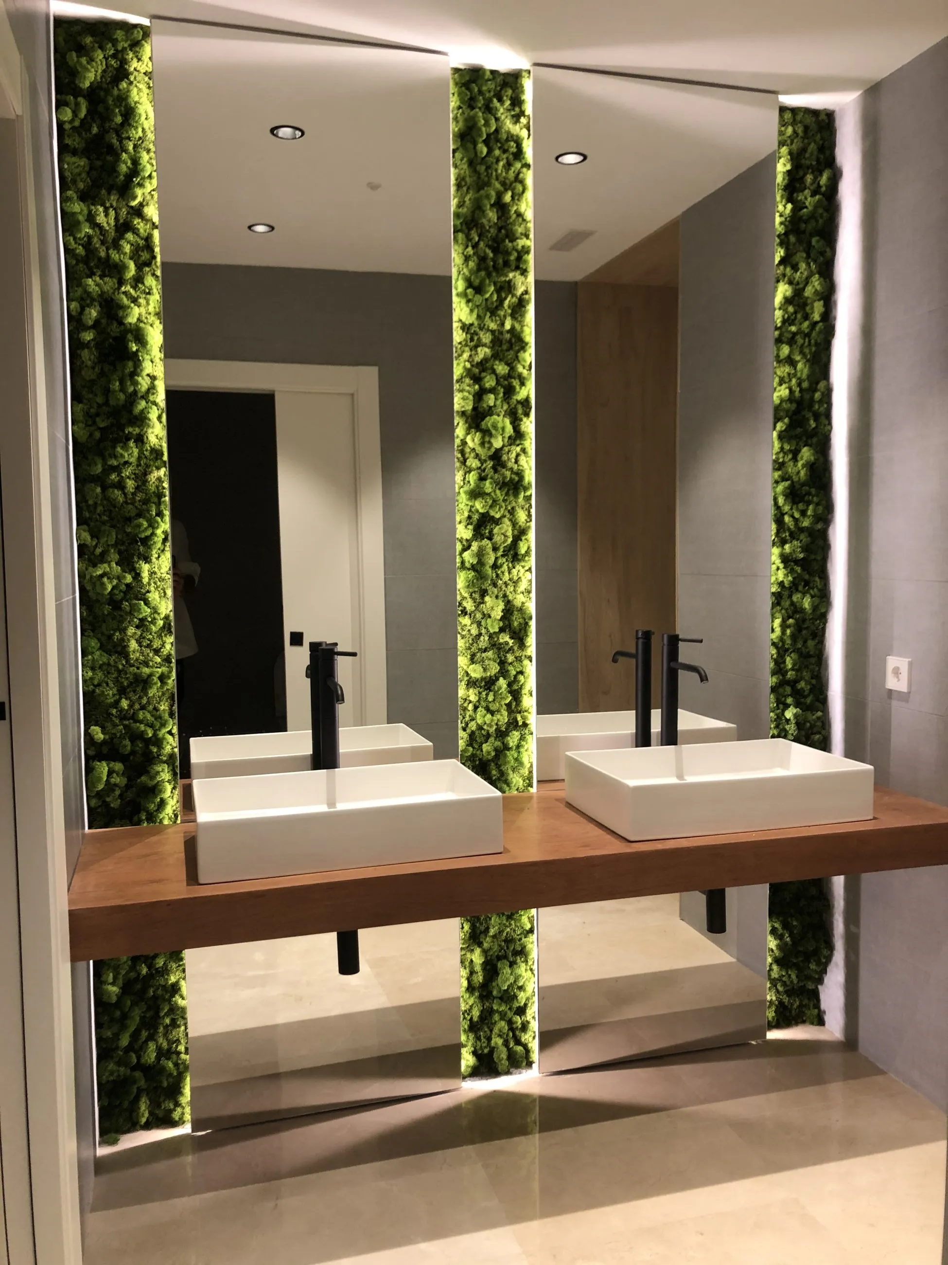Aseo con dos lavabos sobre encimera de madera y columnas de vegetación natural