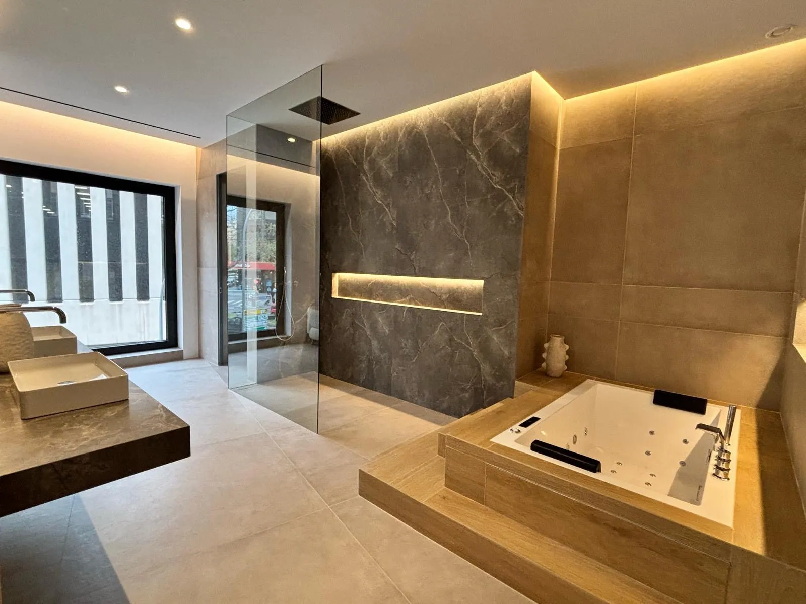 Baño con ducha de piedra gris, bañera sobre plataforma de madera e iluminación integrada, Avenidas
