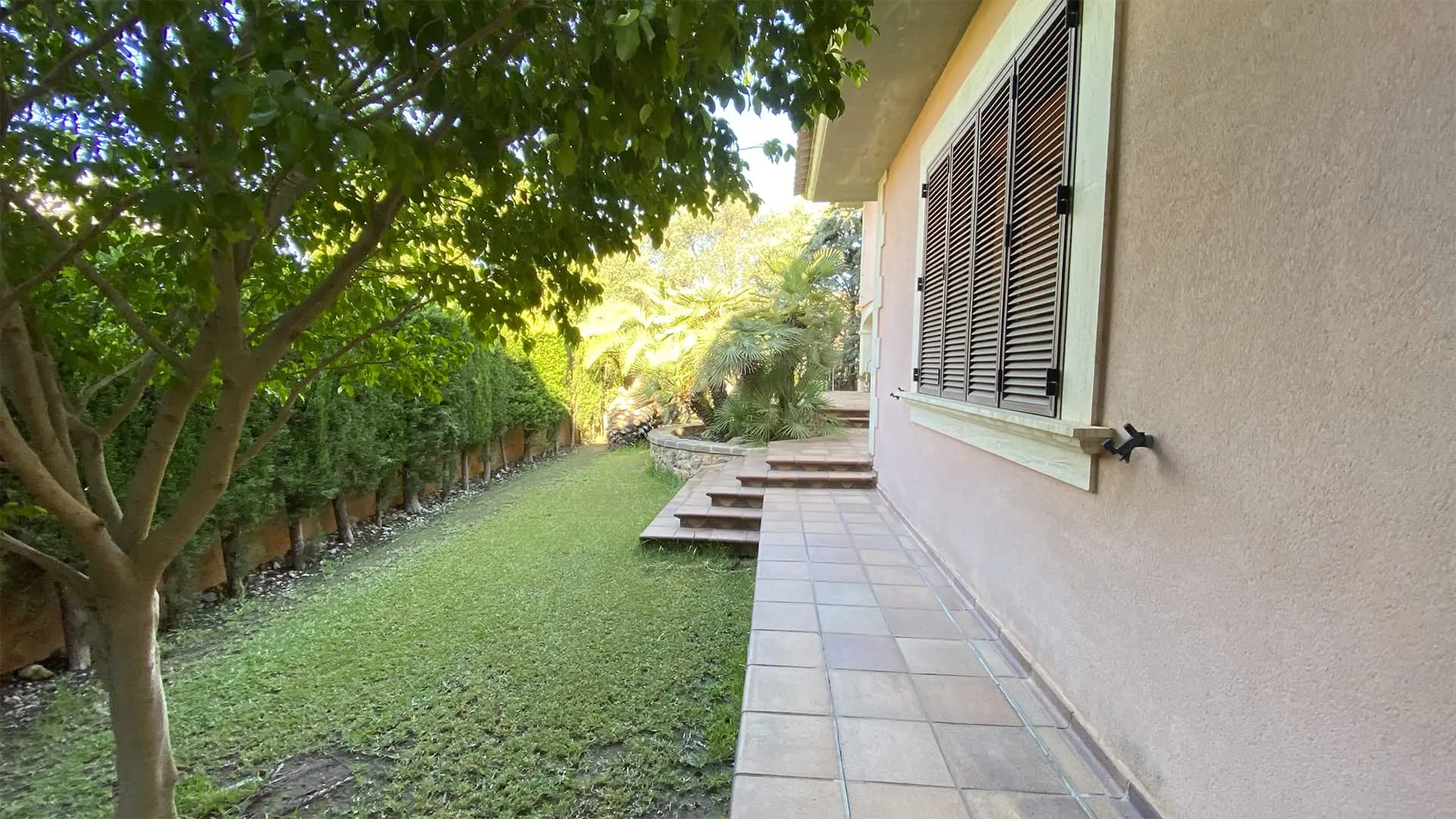 Césped lateral con arbolado y escalera junto a la fachada de la vivienda Xiela, Bunyola