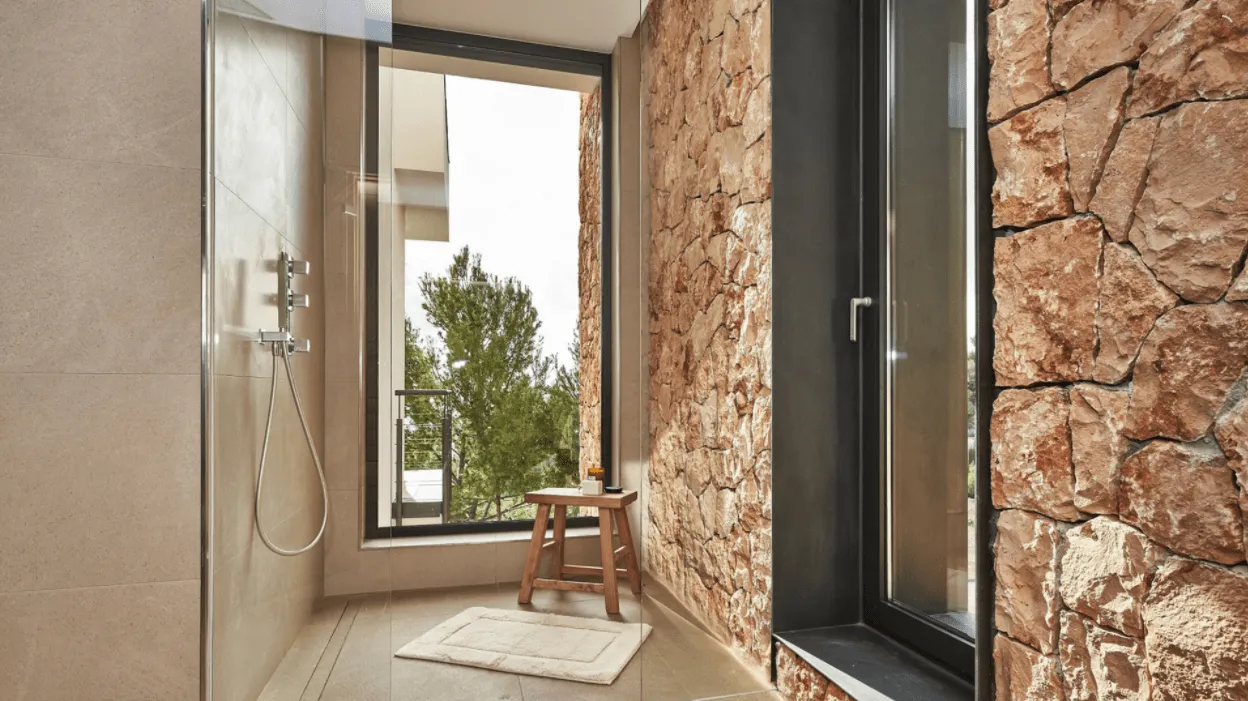 Ducha con ventana vertical y muro de piedra en el baño de la vivienda Génova, Palma