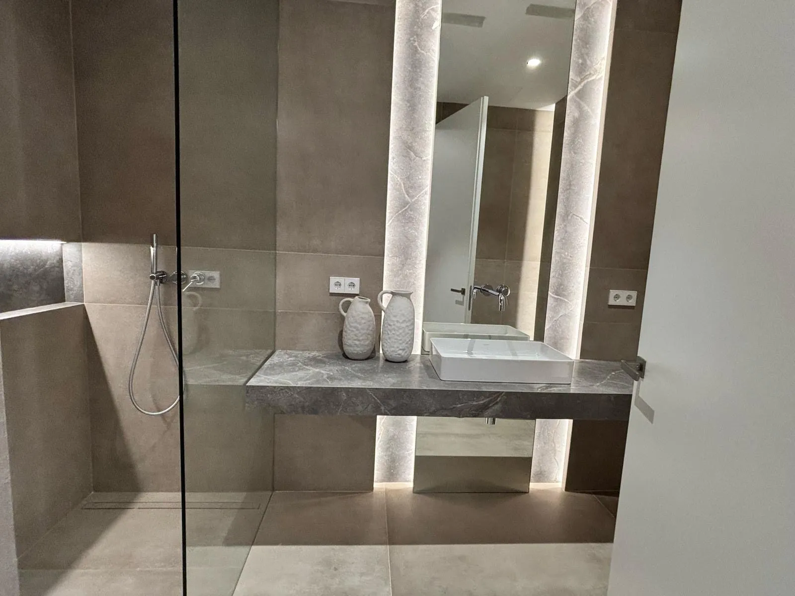 Baño con lavabo de piedra, ducha acristalada y columnas luminosas en la vivienda Avenidas, Palma