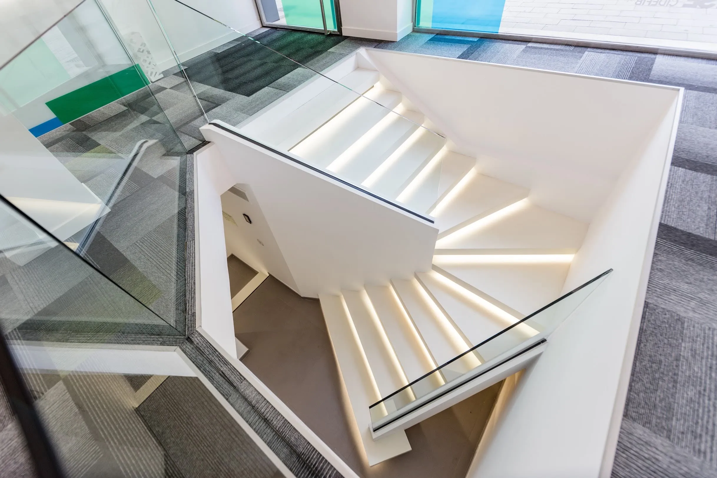Escalera de peldaños iluminados con barandilla de vidrio en la oficina SATSE, Palma