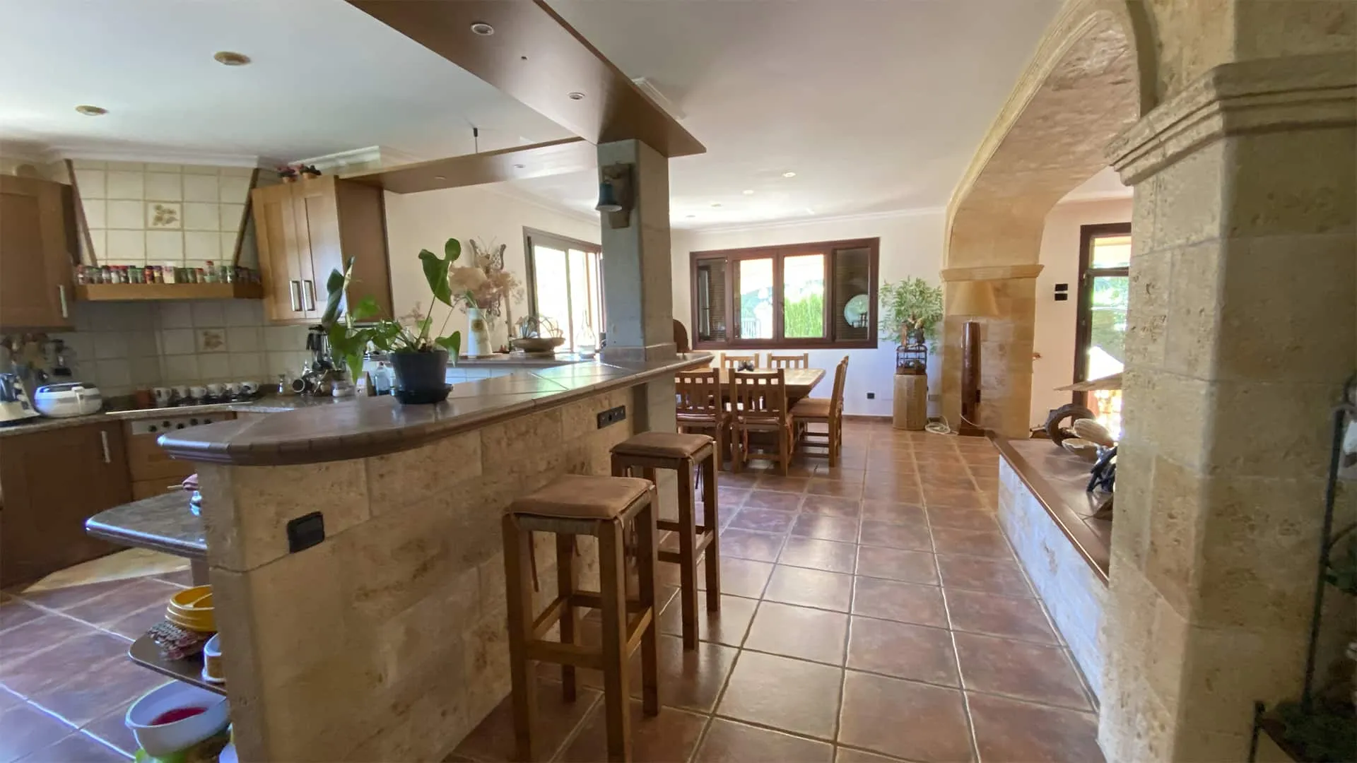 Cocina abierta con barra y taburetes bajo un arco de piedra en la vivienda Xiela, Bunyola