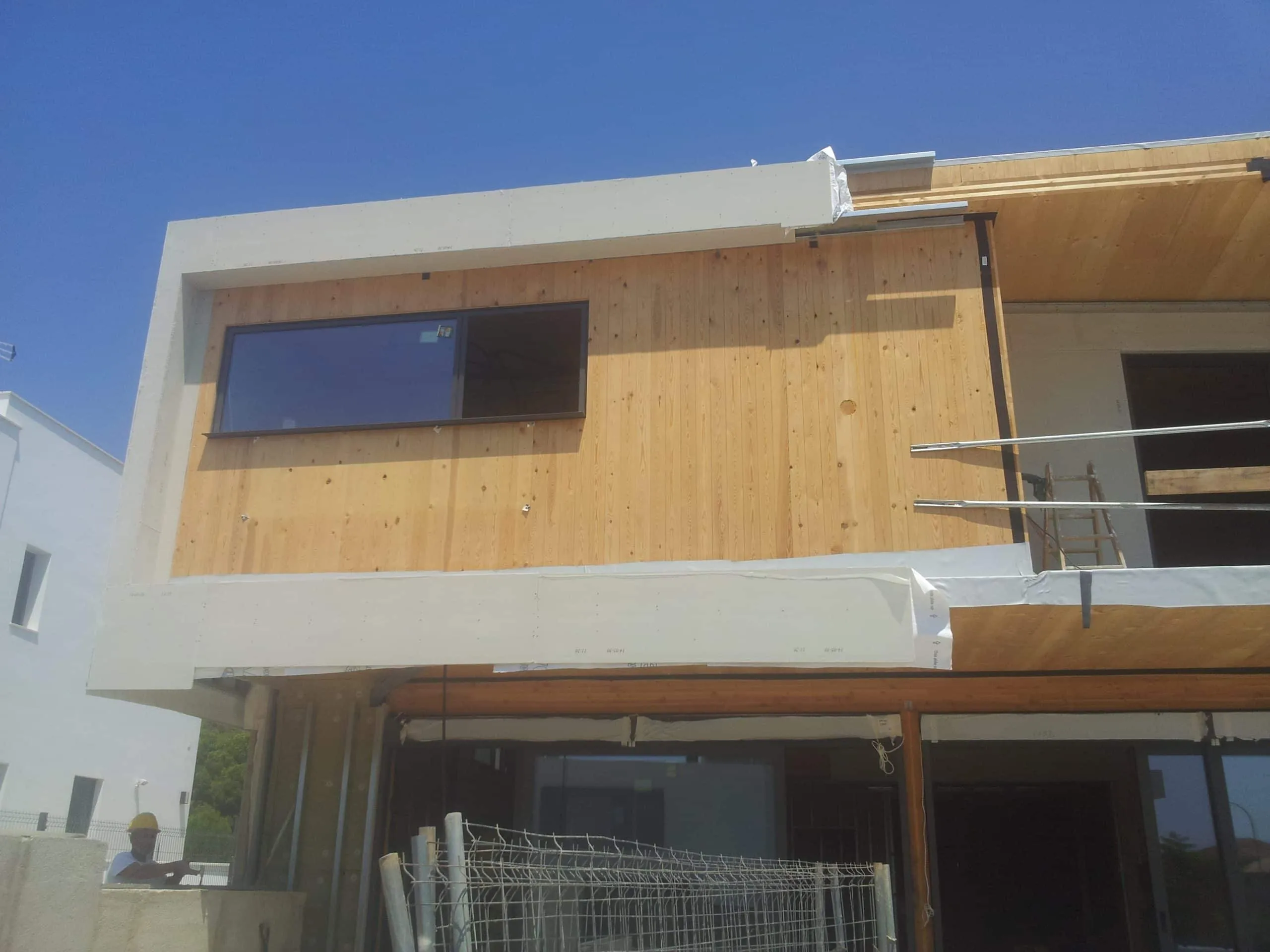Fachada de ADG con revestimiento de madera y marco blanco en fase de obra