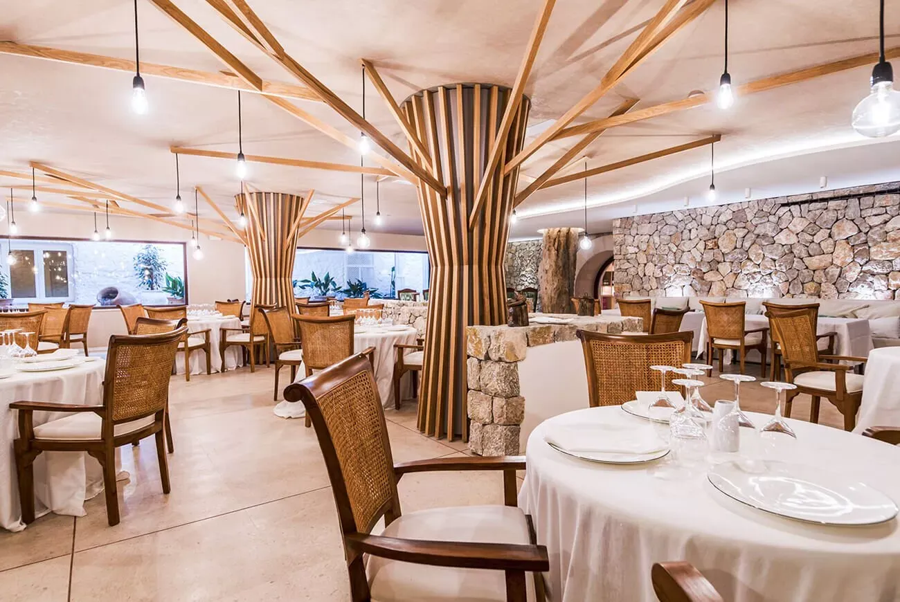 Comedor del hotel Es Ratxó con mesas redondas y estructura de madera