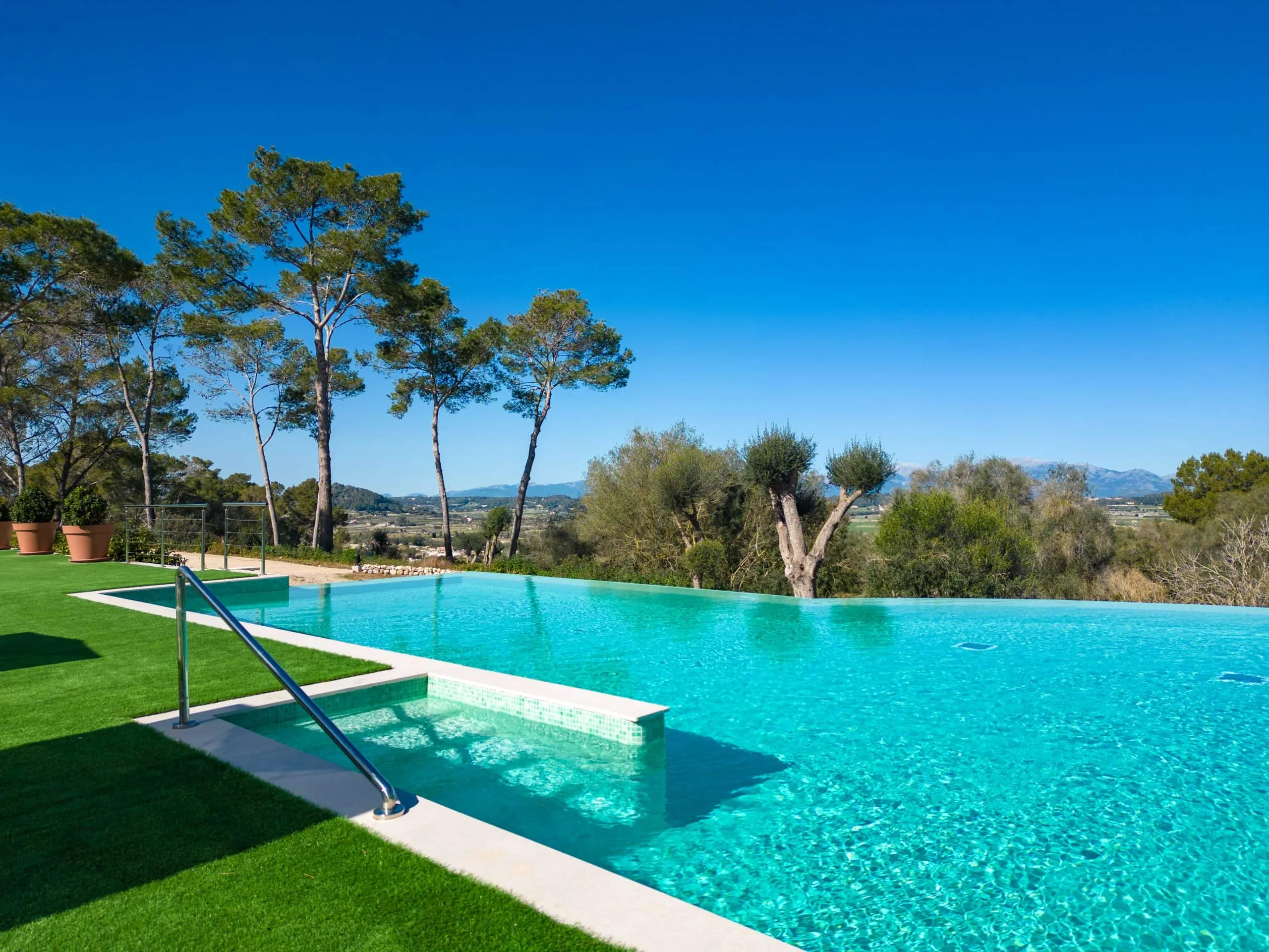 Borde de la piscina exterior del hotel Sa Bastida con césped y pinos, Sant Joan, Mallorca