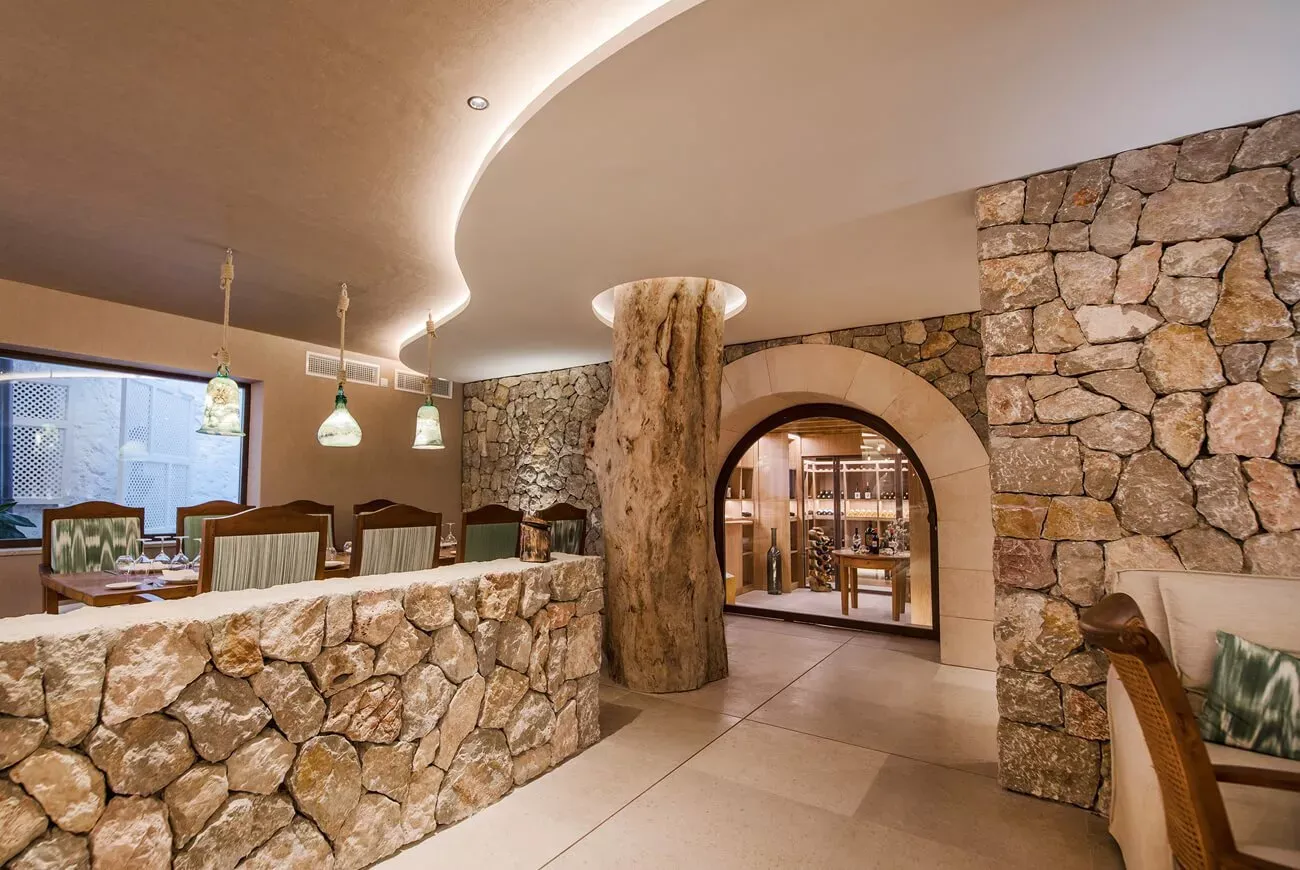 Recepción o bar con muro de piedra y columna de madera, hotel Es Ratxó