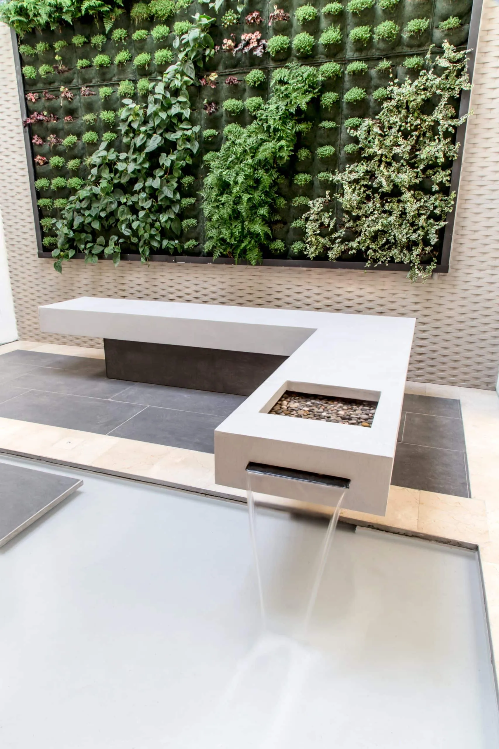 Detalle del banco de hormigón con agua y jardín vertical en el patio de HOMEY, Palma