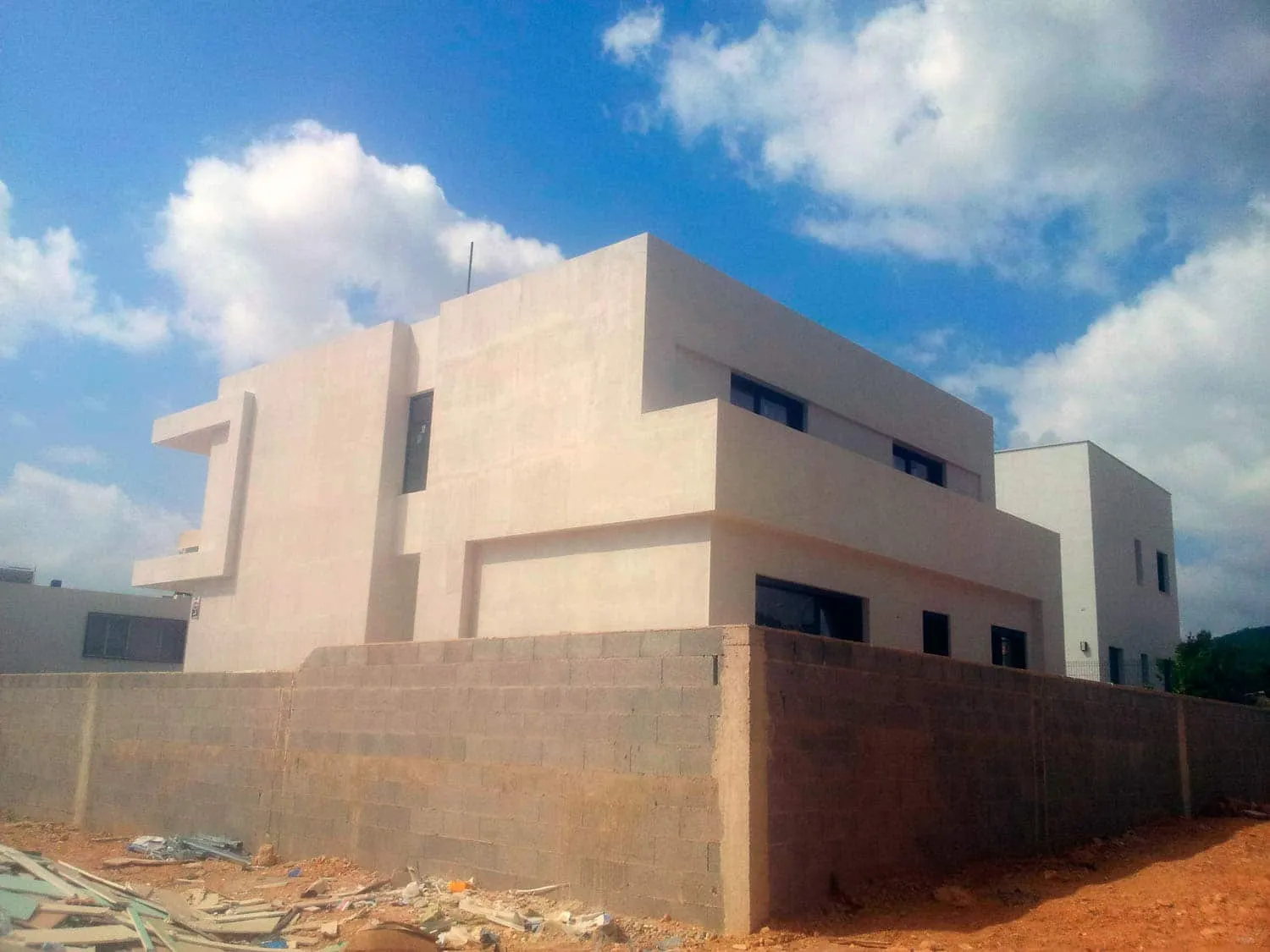 Fachada de ADG con acabado en mortero claro y muro del jardín en obra