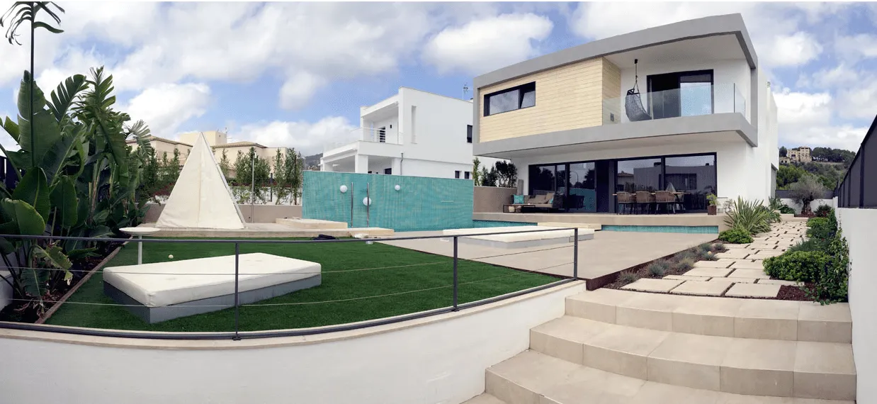 Panorámica del jardín de ADG con césped, escalones, piscina y la fachada de la vivienda